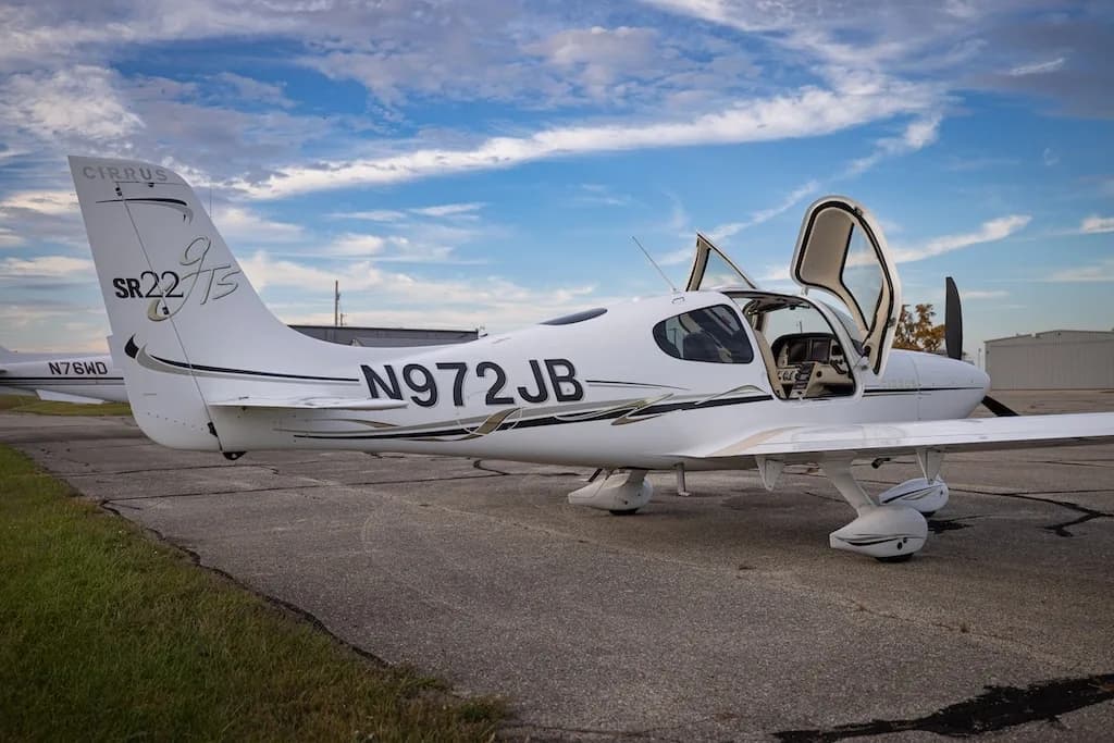 The rear-right side of a white Cirrus SR22T aircraft, N972JB, is shown parked on an airfield with its doors open.