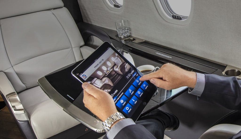 A person using a tablet in the Citation Latitude cabin, with a drink and coffee on the table.