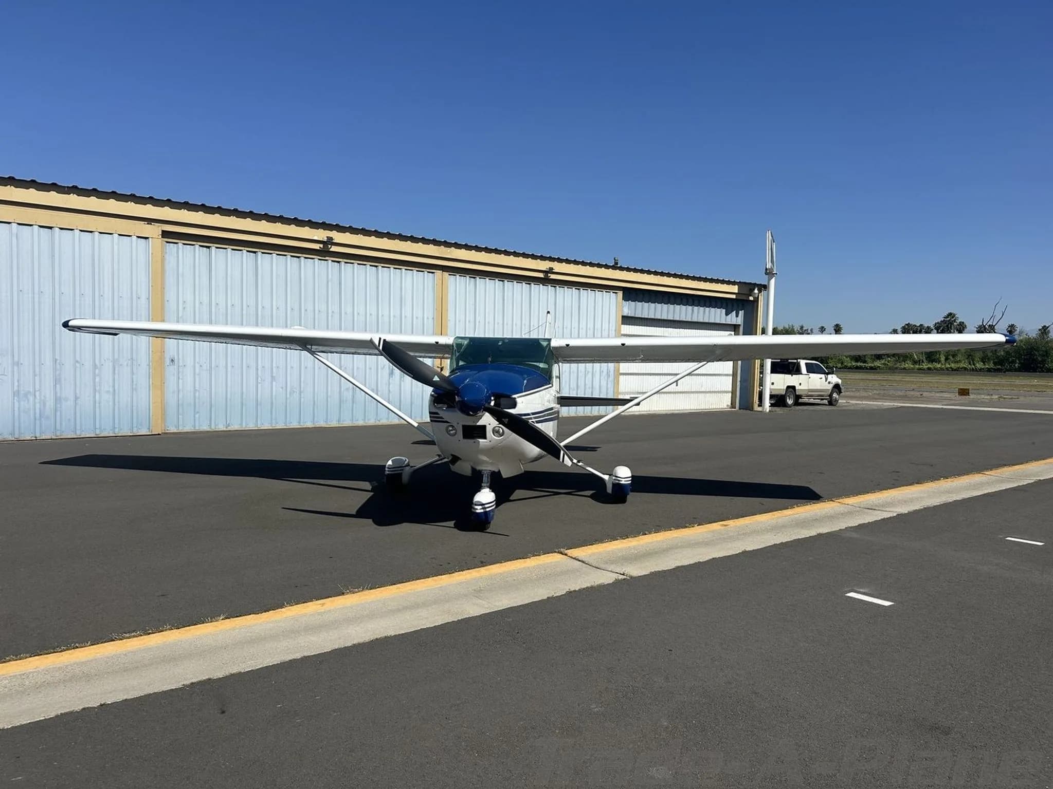 A white and blue Cessna 182 Skylane aircraft parked head-on on an asphalt ramp.