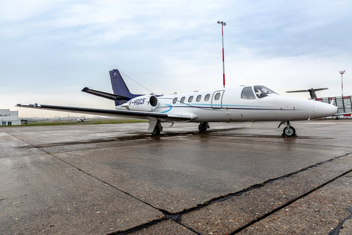 A white and blue Cessna CitationJet (CJ1) with registration F-HGCF parked on a wet tarmac.
