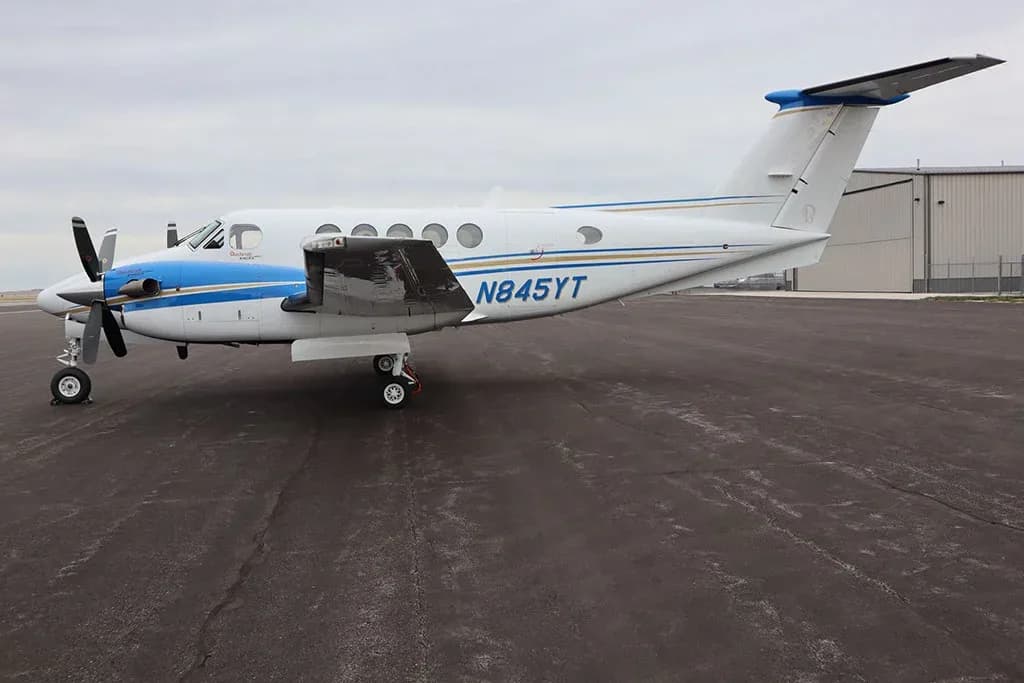 A side view of a white and blue twin-engine turboprop aircraft, N845YT, parked on an asphalt tarmac.