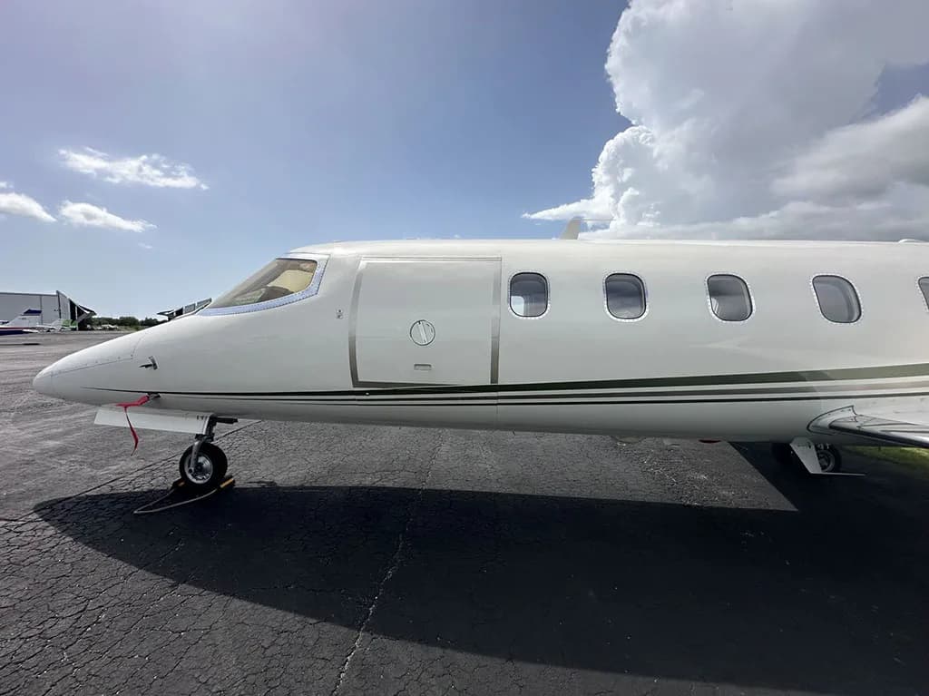 A close-up side view of the front fuselage of a white Learjet 35A with green and gold stripes.