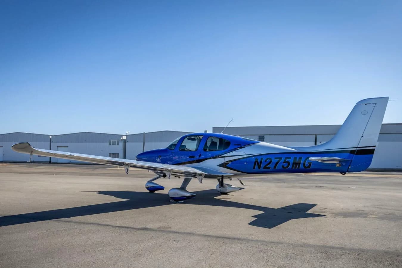 A side view of the blue and silver Cirrus SR22 aircraft, N275MG, parked on an airport tarmac.