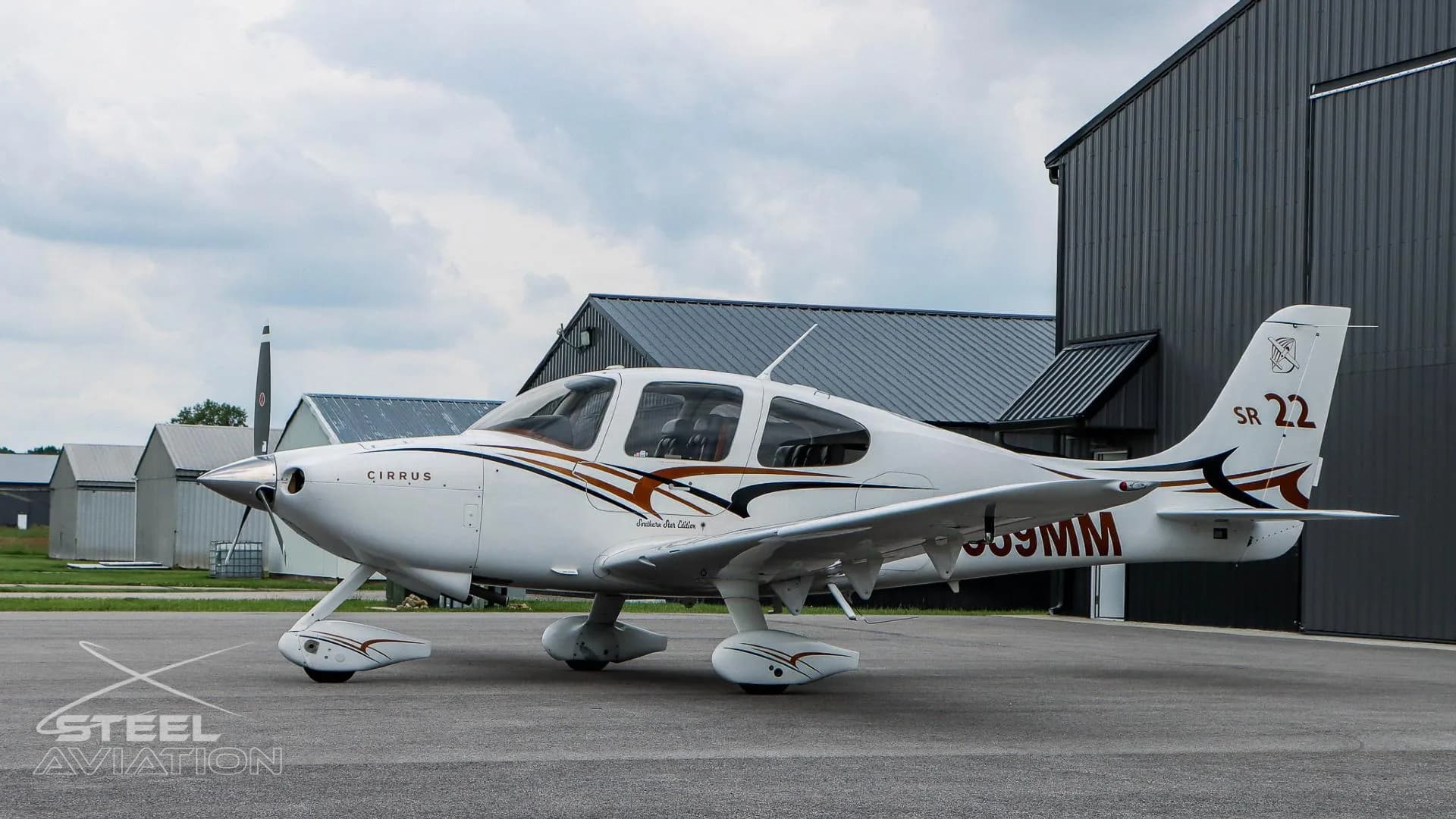 A white Cirrus SR22 aircraft with N559MM registration is parked on an airfield with hangars in the background.