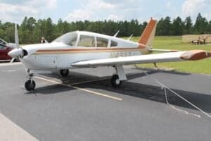 A white and orange Piper PA-28 Cherokee parked on the tarmac.