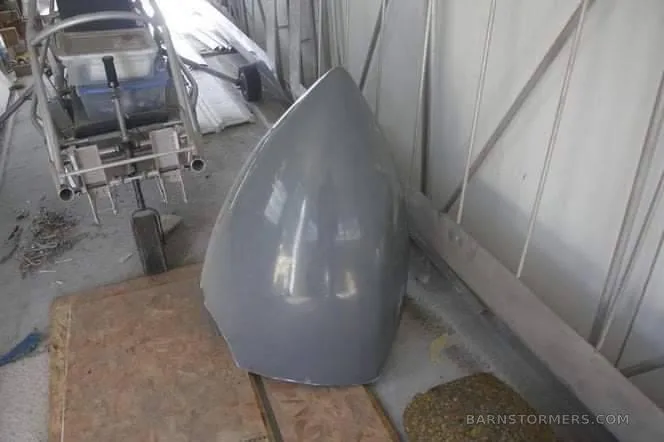 A close-up of a shiny grey aircraft nose cone or fairing on a wooden surface in a workshop.