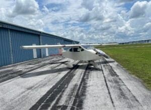 A white aircraft is parked on the tarmac in front of a blue hangar.