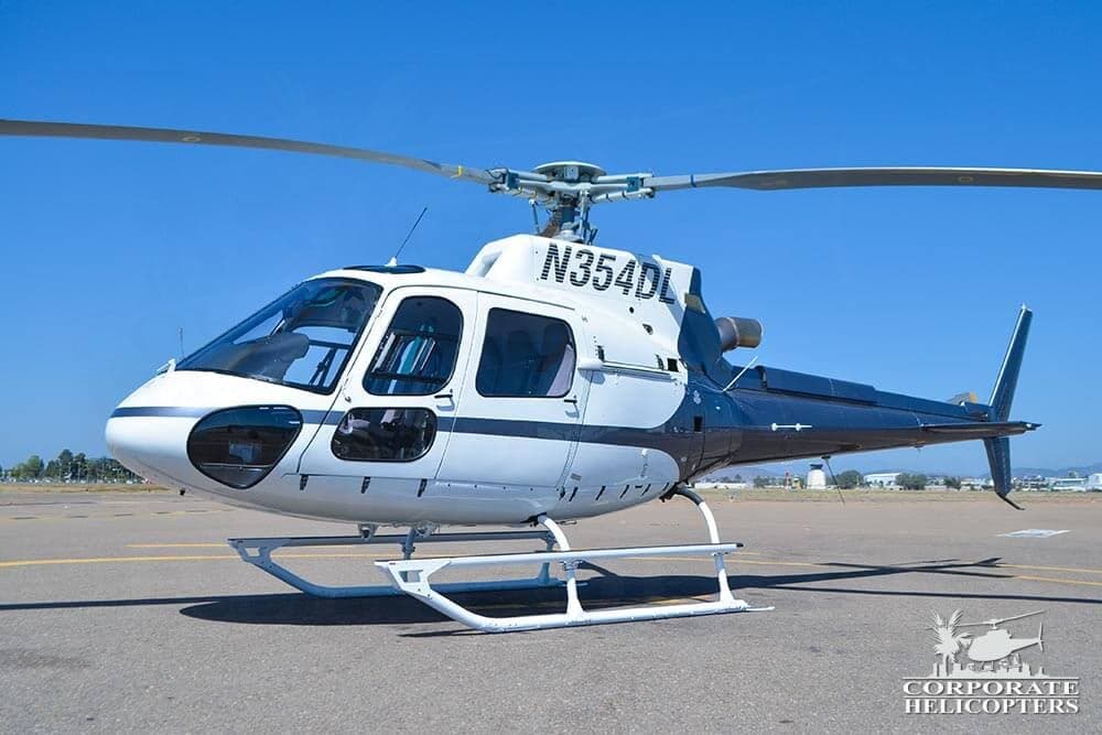 A white and dark blue helicopter, registration N354DL, parked on an airfield under a clear blue sky.