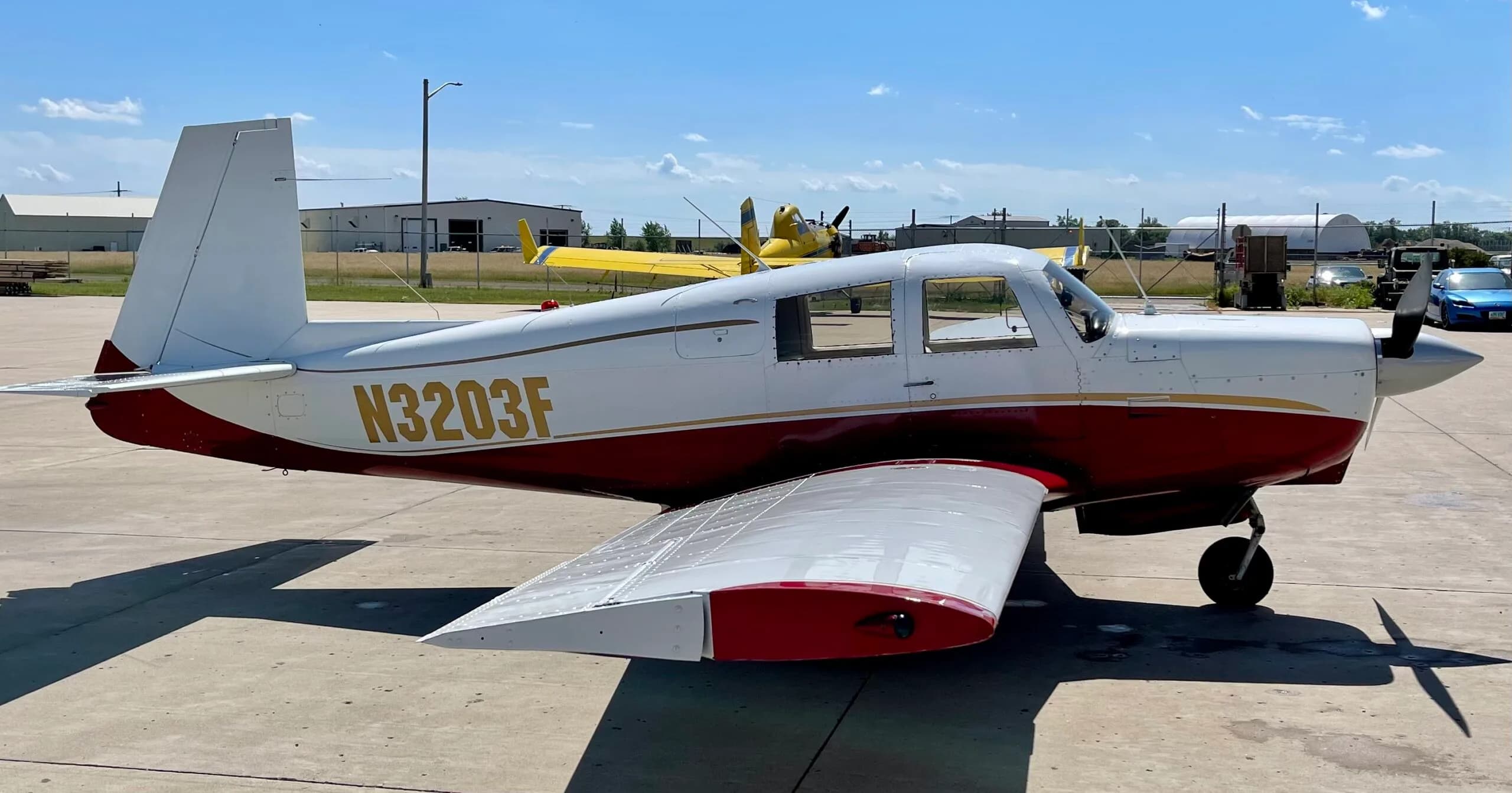 A white and red single-engine propeller aircraft with registration N3203F parked on an airfield, with other aircraft and hangars in the background.