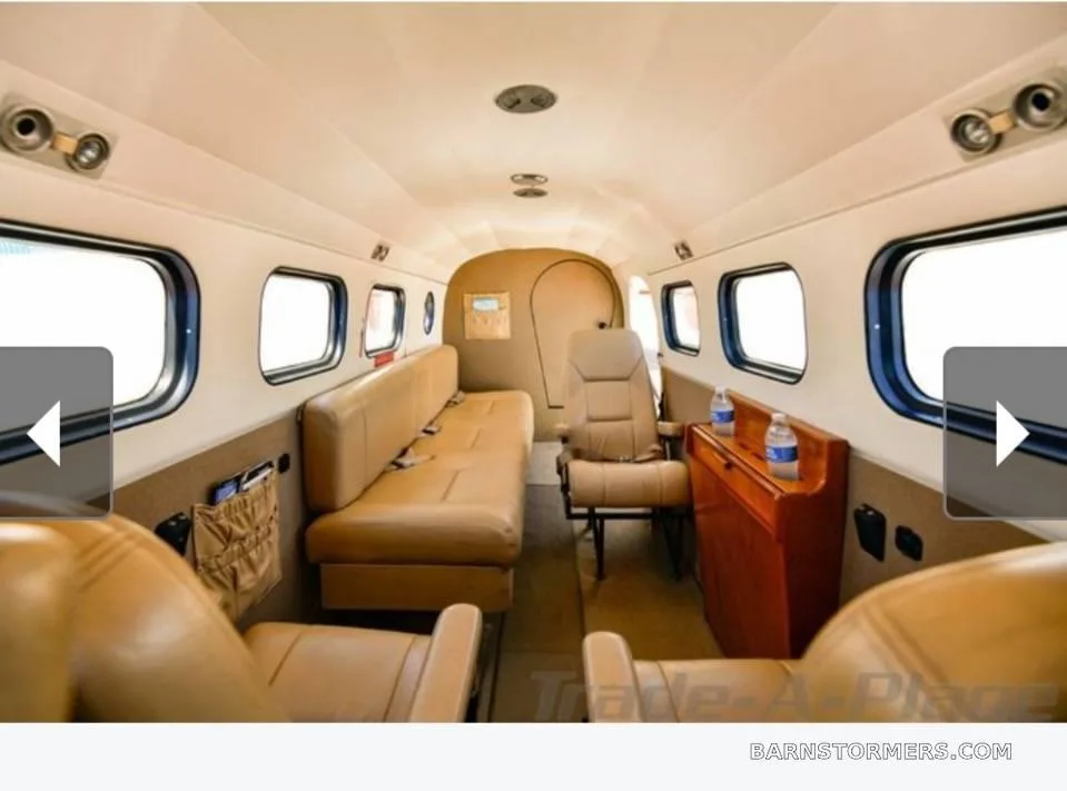 The interior cabin of an aircraft with tan leather seating, a wooden cabinet, and multiple windows.