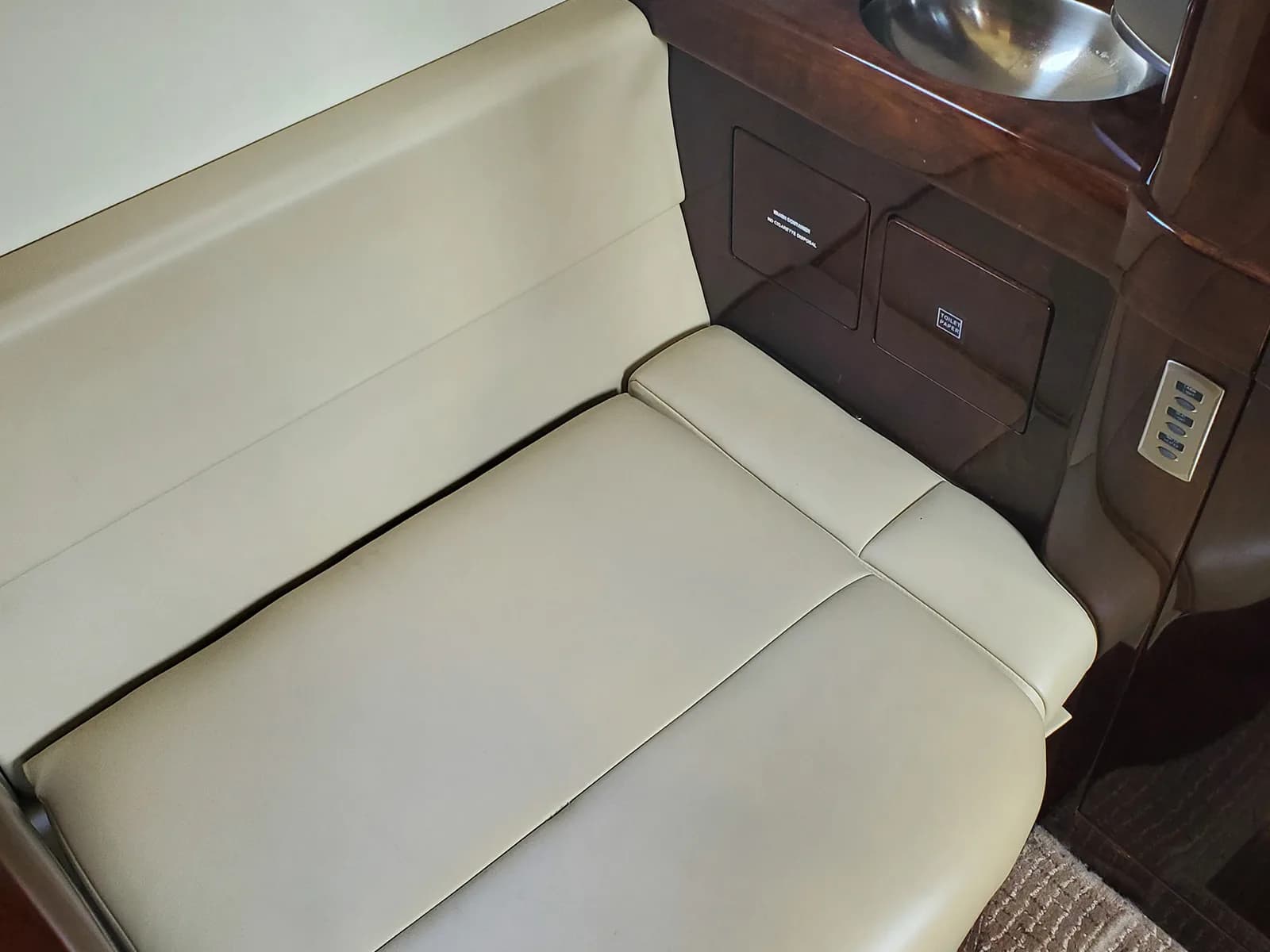 A light beige leather seat next to a dark wood cabinet with a small sink in an aircraft cabin.