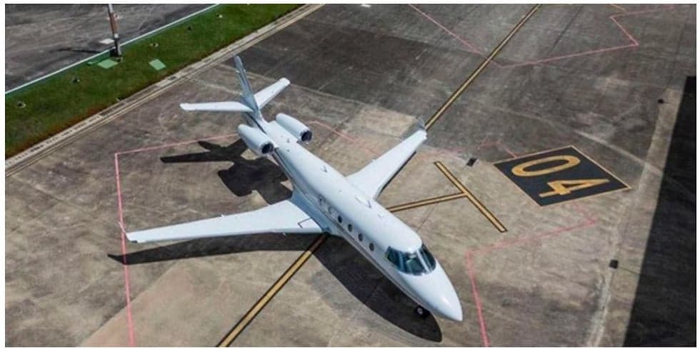 An aerial view of a white jet aircraft parked on a tarmac with yellow markings.