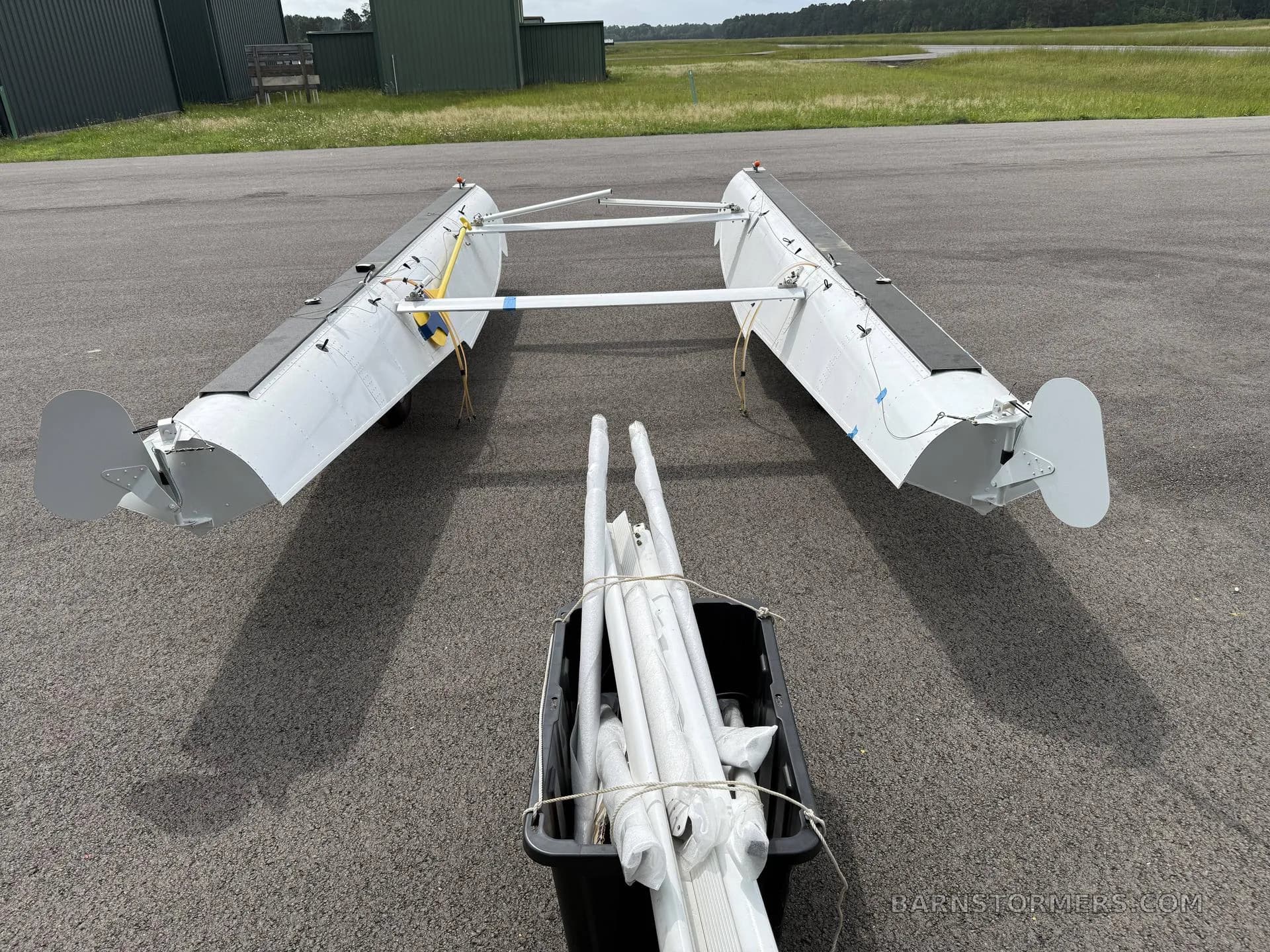 An overhead view of two white aircraft floats with wheels and a bin of struts on an asphalt apron.