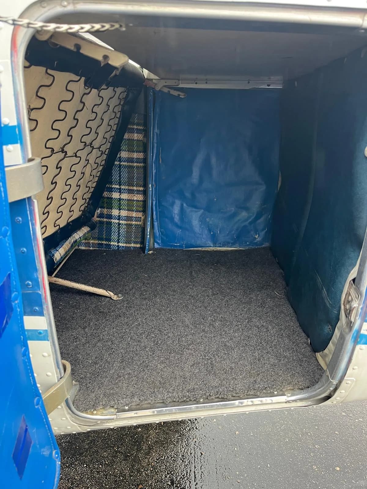 The cargo area of a Cessna 172, showing a blue carpeted floor and plaid fabric on the side.