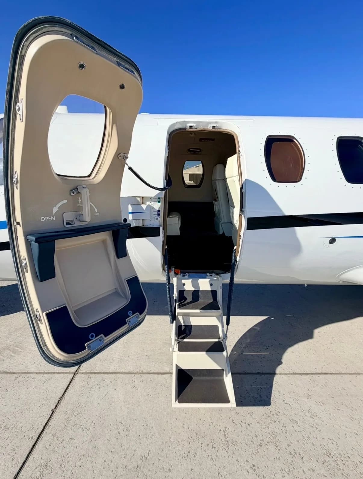 The main entry door of a white Cessna CitationJet is open, revealing the integrated steps leading into the cabin.