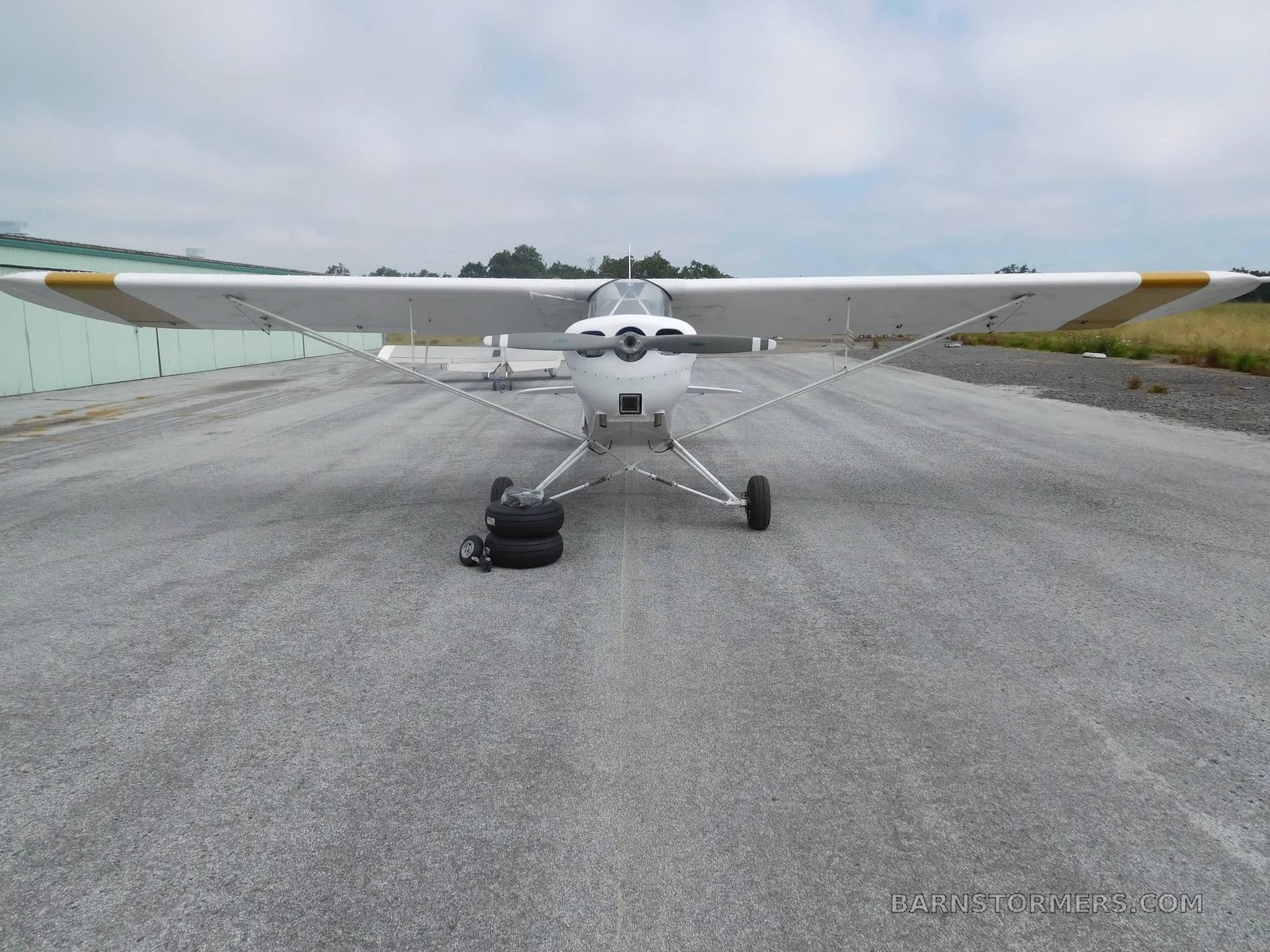 The front view of a white experimental aircraft with gold wing stripes, parked on an asphalt runway.