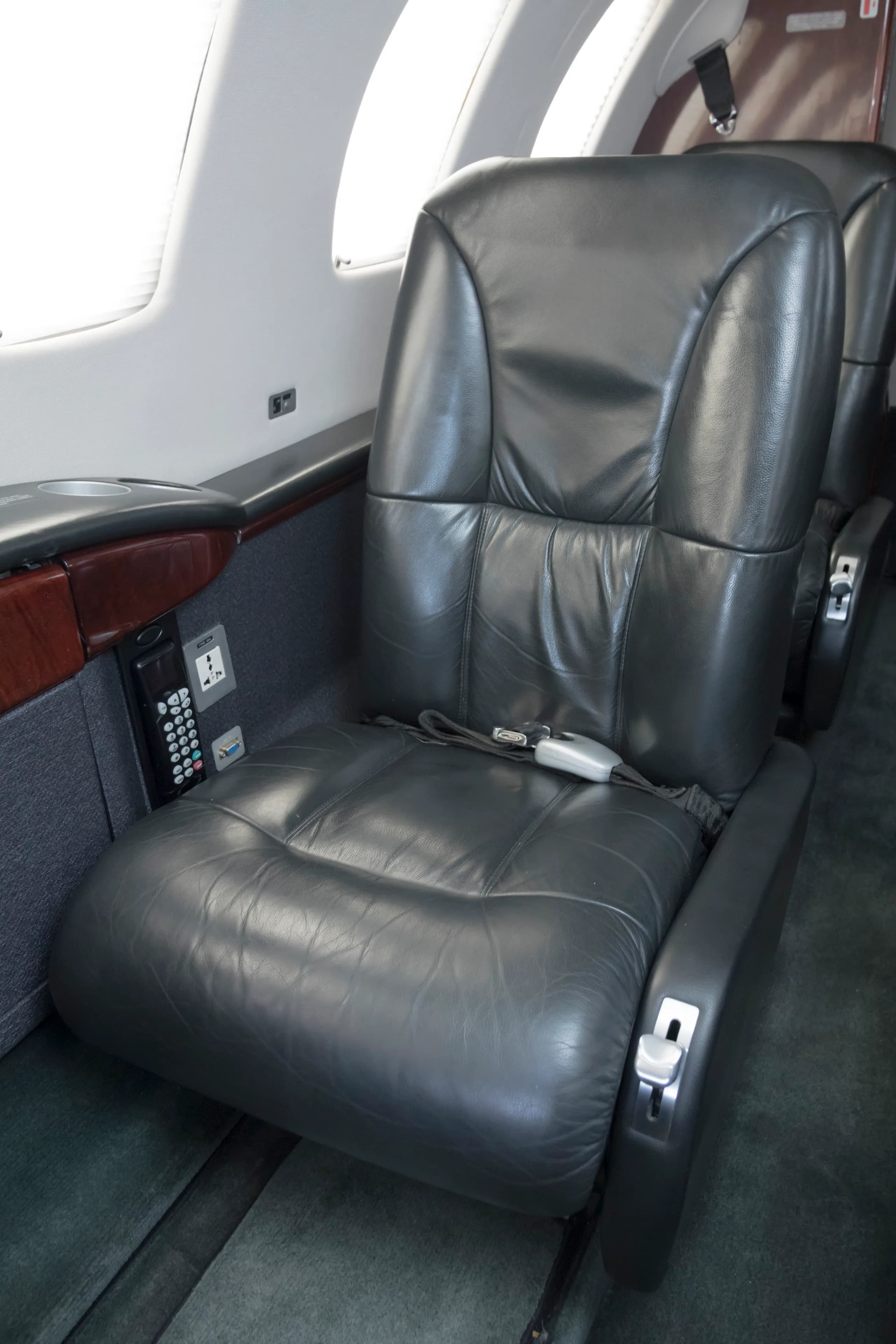 A close-up of a black leather passenger seat in a private jet cabin, with a control panel on the side.