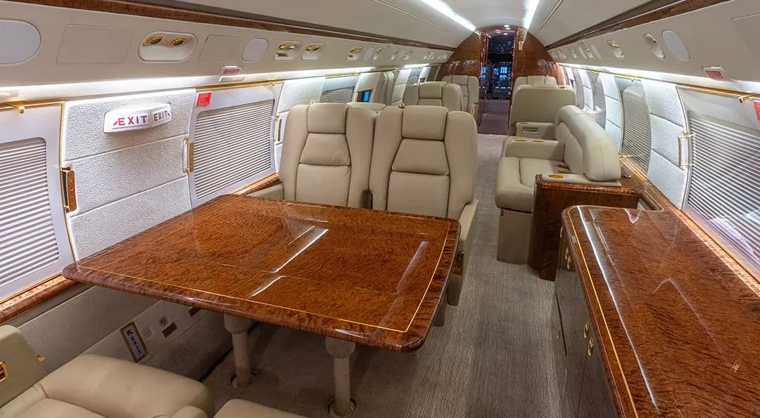 A wide view of the business jet's cabin, showcasing a dining table and comfortable beige leather seating.