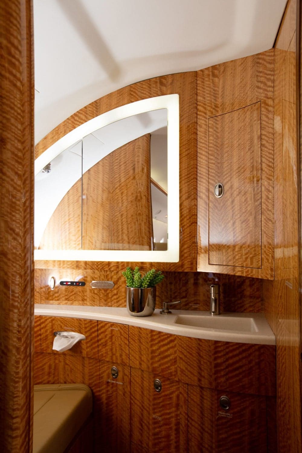 A luxurious aircraft lavatory with wood paneling, a sink, and an illuminated mirror.