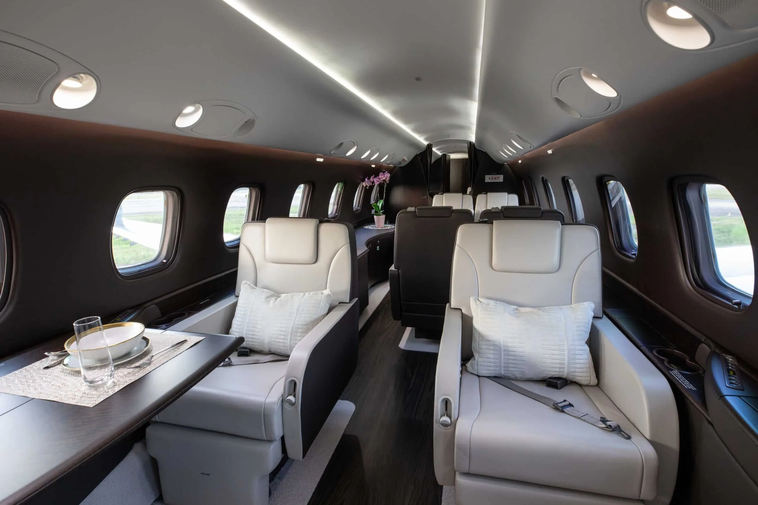 The aircraft's luxurious cabin with light leather seats, a table set for dining, and dark wood flooring.