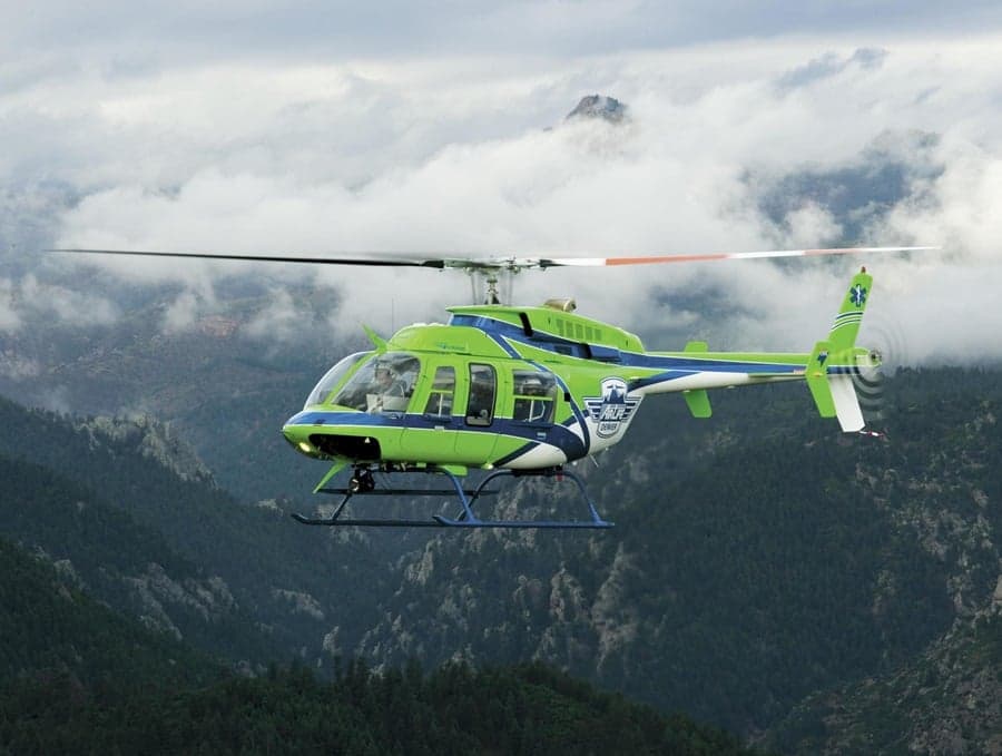 Green and blue air ambulance helicopter flying over a mountainous landscape.
