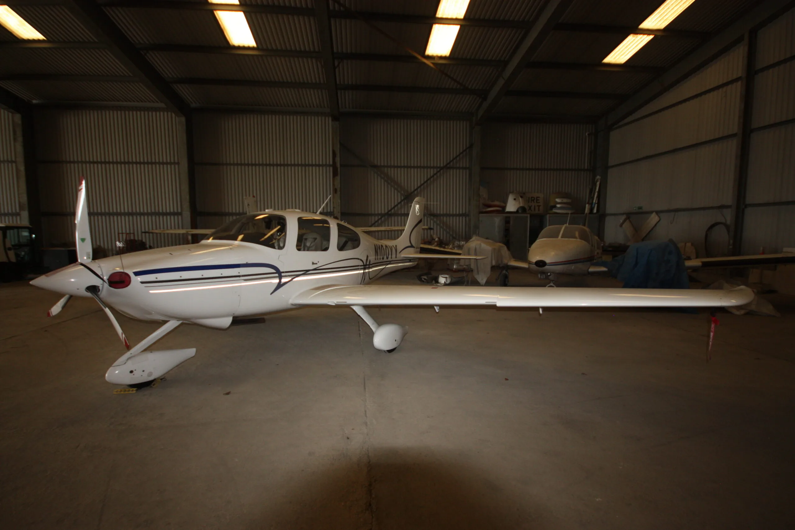 A white Cirrus SR22 aircraft with blue and grey stripes parked inside a hangar.