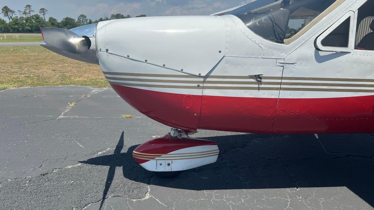 A close-up side view of the aircraft's nose and front landing gear, showing the red and white paint with gold stripes.
