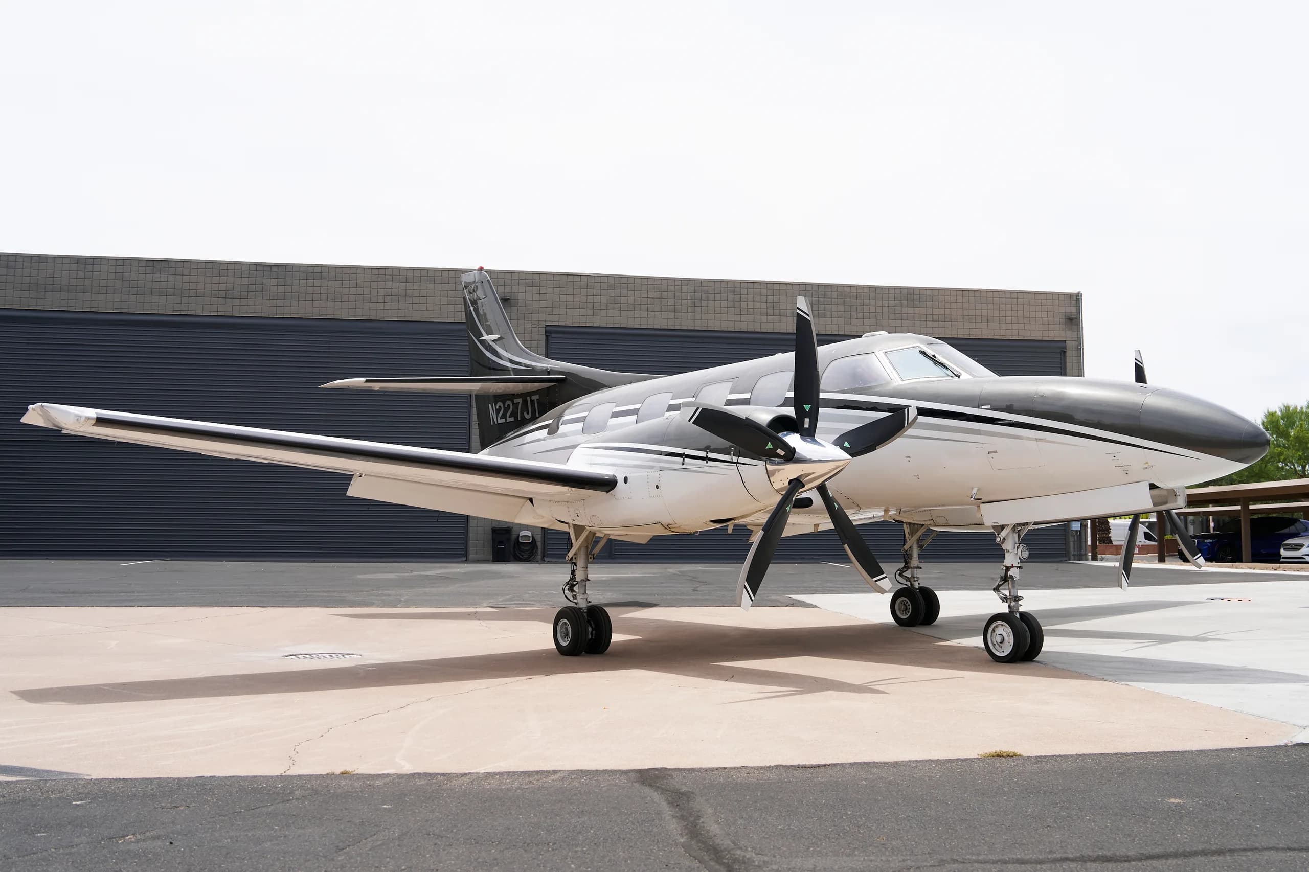 A white and black twin-engine turboprop aircraft, N227JT, parked on a tarmac with a hangar in the background.