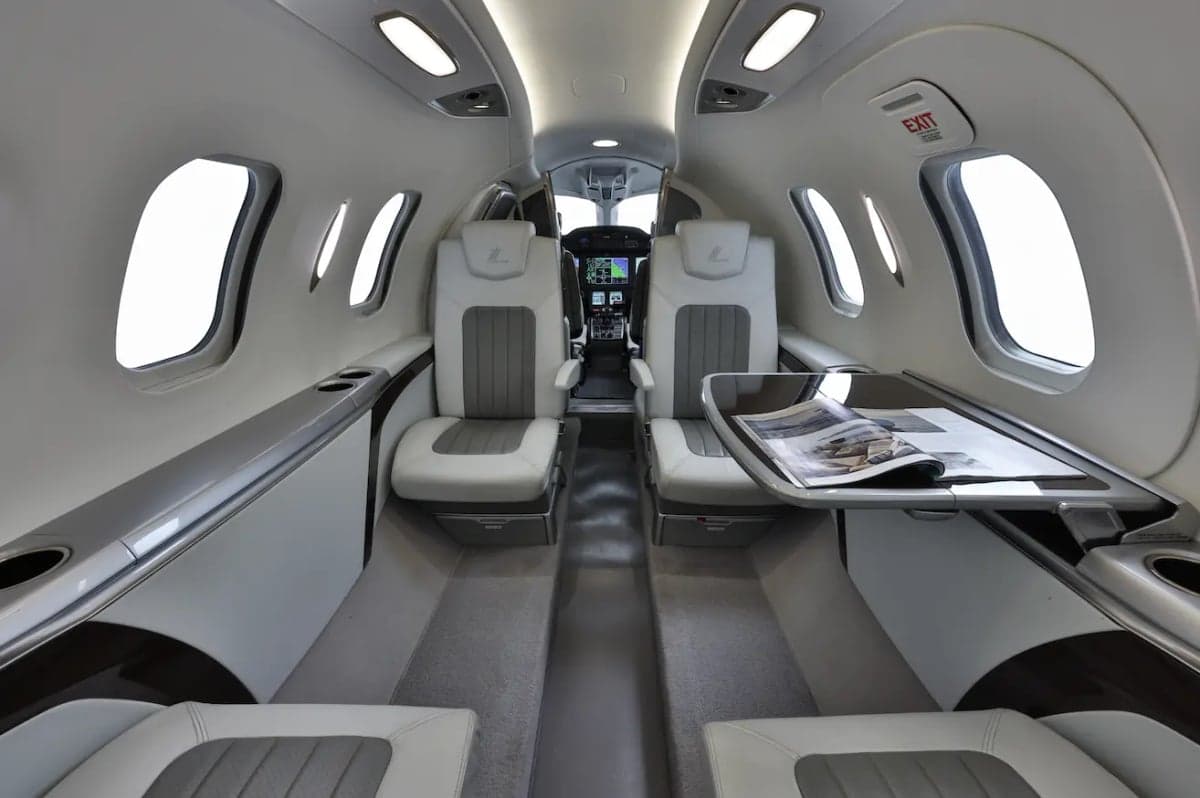 The luxurious cabin interior of a HondaJet HA-420, featuring light gray and white leather seats and a fold-out table.