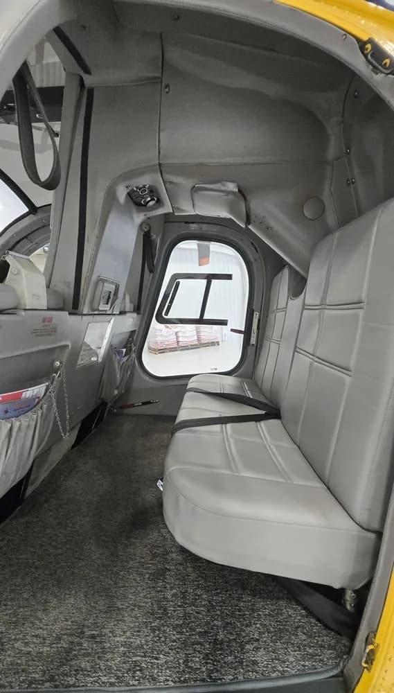 The rear cabin interior of the helicopter, featuring grey bench seating and a side window.