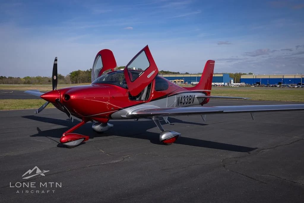 A three-quarter front view of the red and silver Cirrus SR22 aircraft N433BV with its doors open, parked on an airfield.