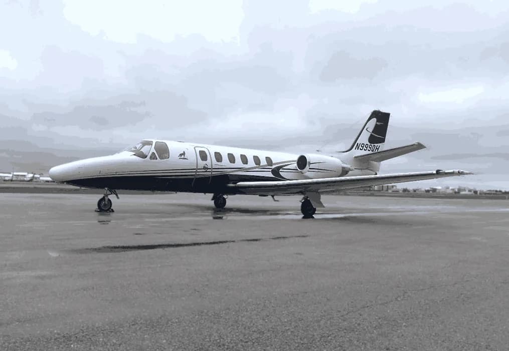 A white and black business jet, registration N9990H, parked on a wet tarmac under a cloudy sky.