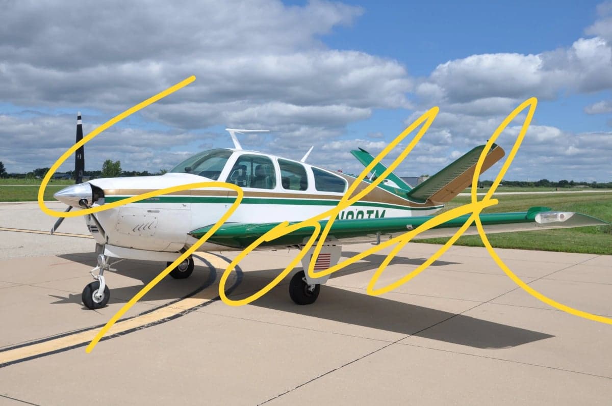 A Beechcraft Bonanza aircraft with a white and green paint scheme is parked on the tarmac, with the word "SOLD" overlaid.