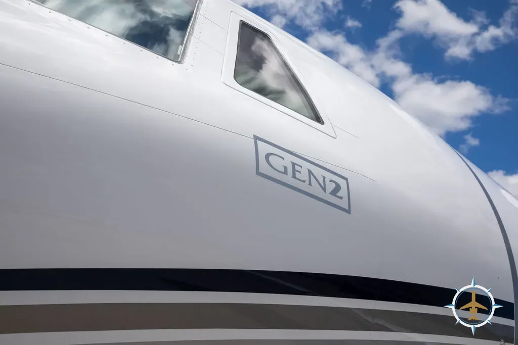 A close-up of the white fuselage of a business jet, showing 'GEN2' text and cockpit windows against a blue sky.