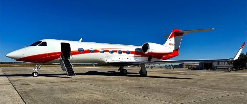 A white Gulfstream G650 aircraft with red stripes parked on the tarmac with its door open and stairs deployed.