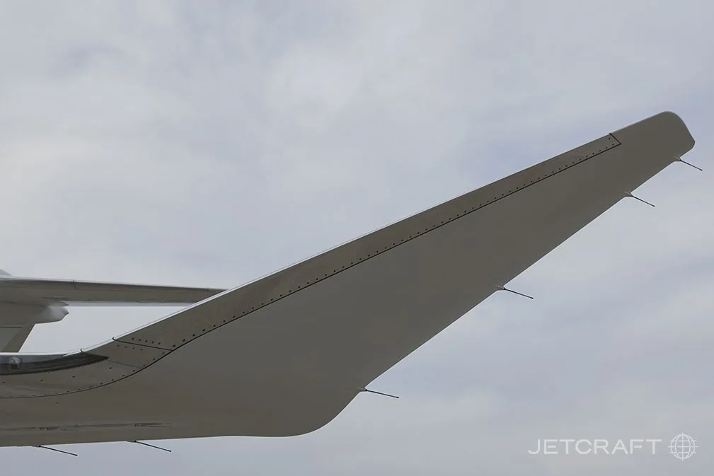 A close-up view of the wingtip of a white Bombardier Global 7500 business jet against a cloudy sky.