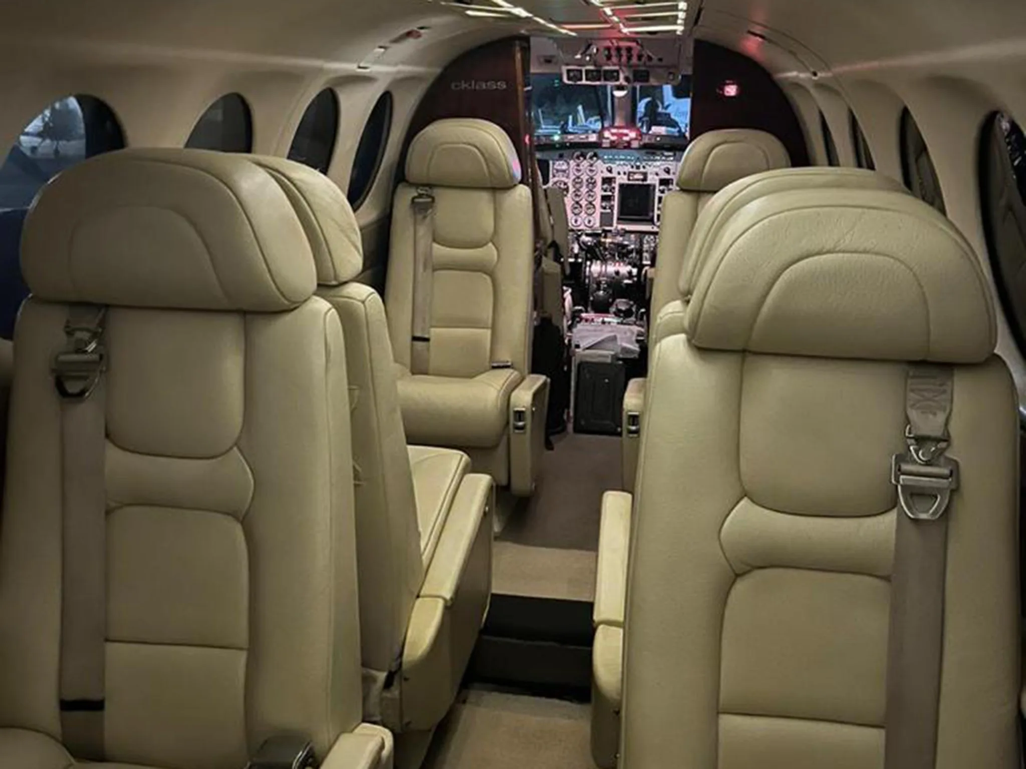 The interior cabin of an aircraft, showing rows of light-colored leather seats looking towards the cockpit.