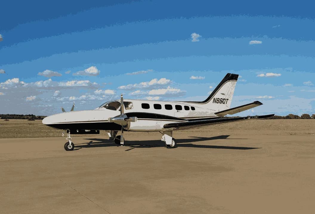 A white twin-engine Cessna 414 Chancellor with black stripes is parked on a tarmac under a blue sky.