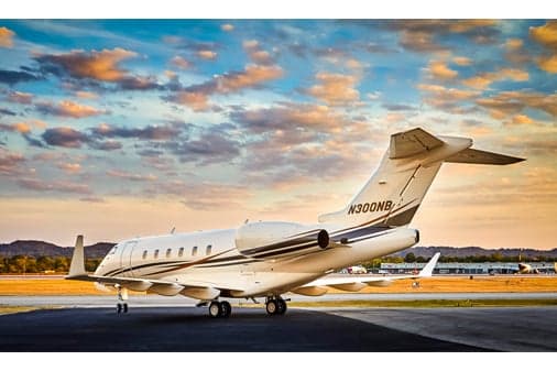 A rear view of a white business jet with dark and gold stripes, registration N300NB, parked on a tarmac at sunset.
