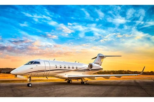 A white business jet with dark and gold stripes, registration N300NB, parked on a tarmac at sunset.