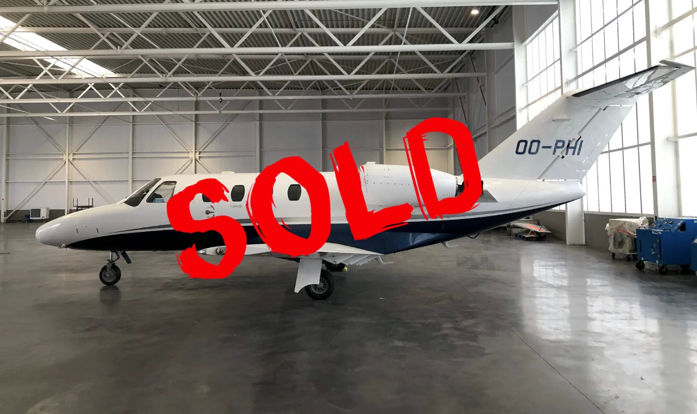 A white and blue Cessna CitationJet business jet is parked inside a hangar, viewed from the side.