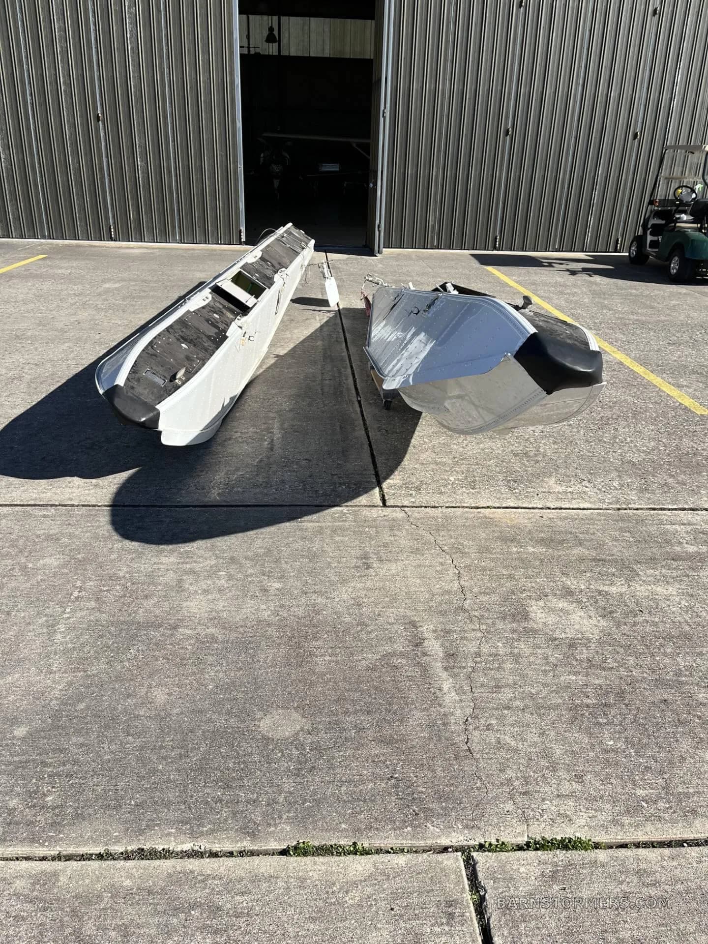 Two white aircraft floats with black tips lying on a concrete apron in front of a hangar.
