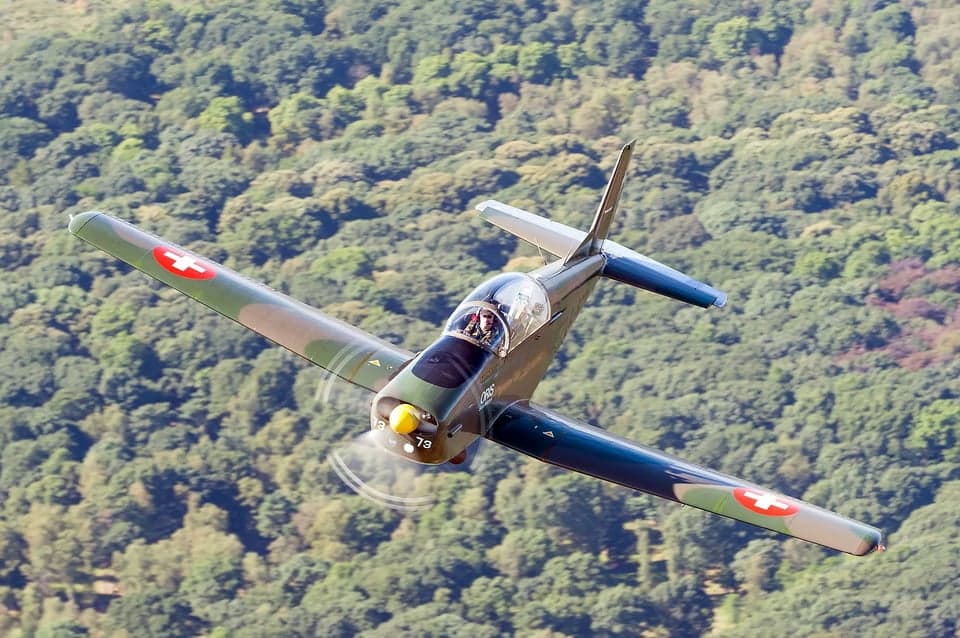 Pilatus PC-7 in flight over a town and lake.