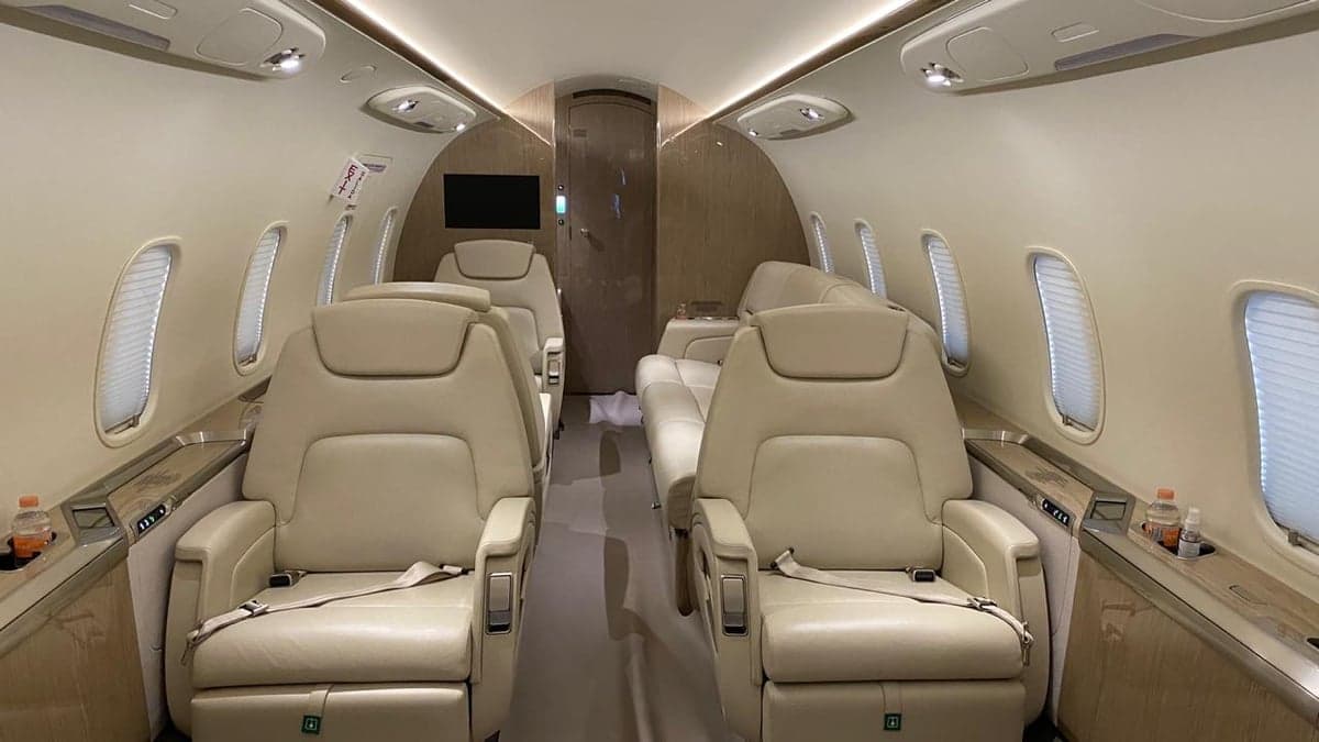 View of the aircraft cabin with cream-colored leather seats and a TV screen.