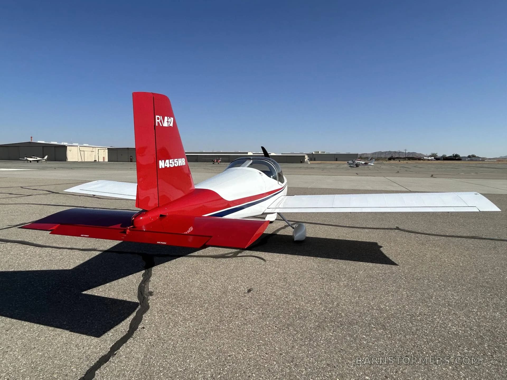 A white and red Van's RV-7 aircraft, registration N455HR, is parked on an asphalt tarmac, viewed from the rear-right side.