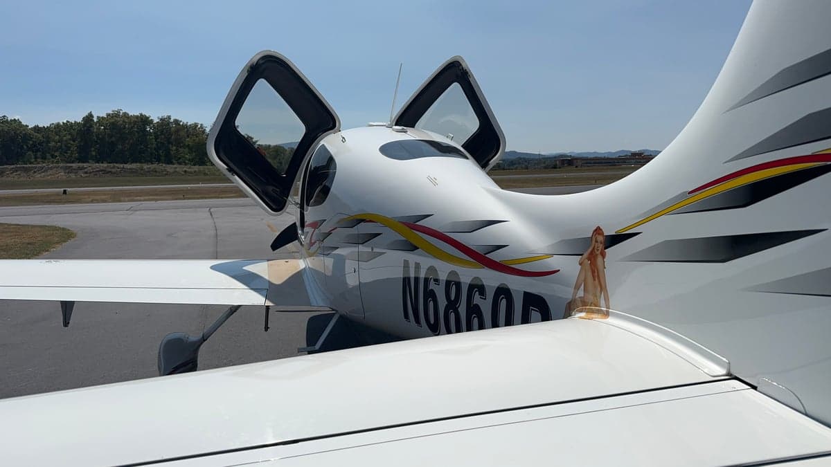 Rear view of a Cirrus aircraft with its doors open, showing the registration number N6869R and custom graphics.