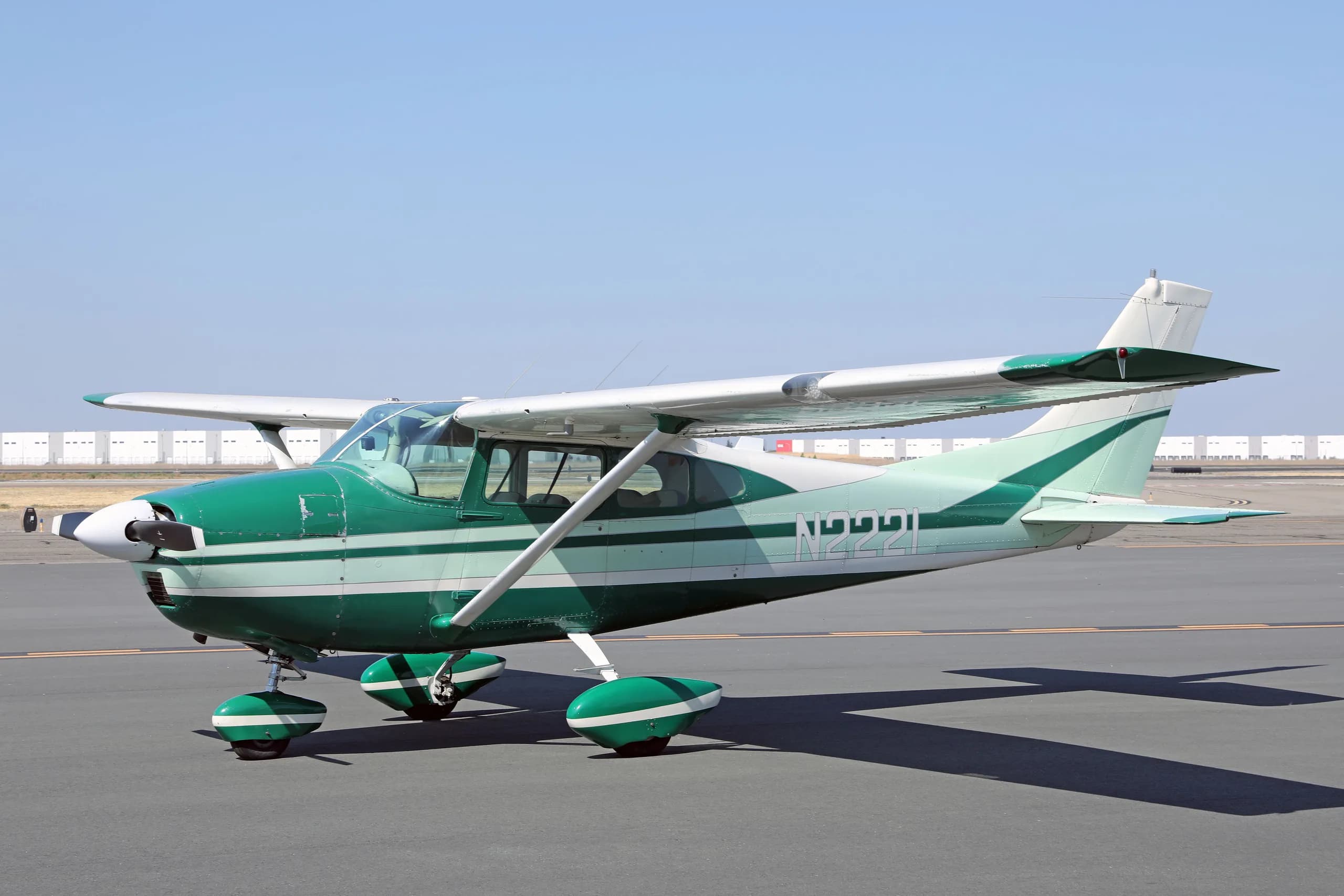 A side view of a green and white Cessna 182 Skylane N2221 on an airfield tarmac.