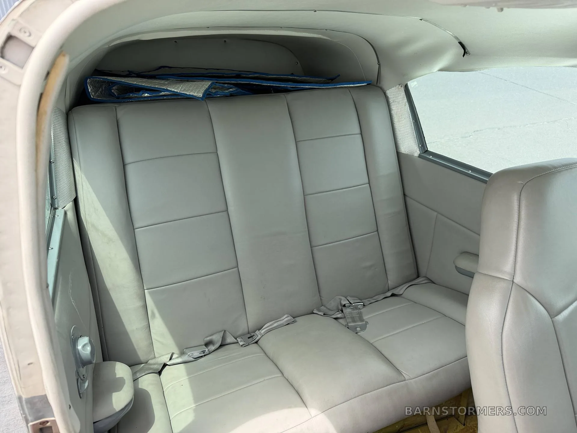 The light gray leather rear bench seat of a small aircraft cabin.