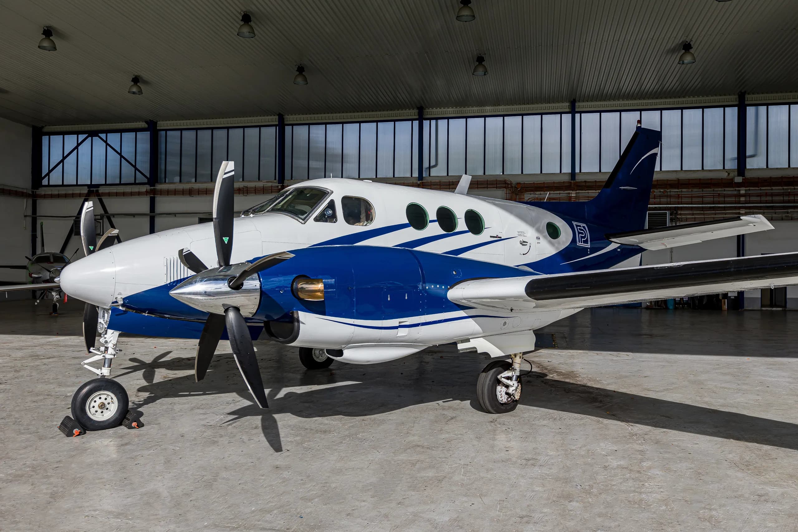 A white and blue twin-engine turboprop aircraft, likely a King Air, parked inside a hangar.