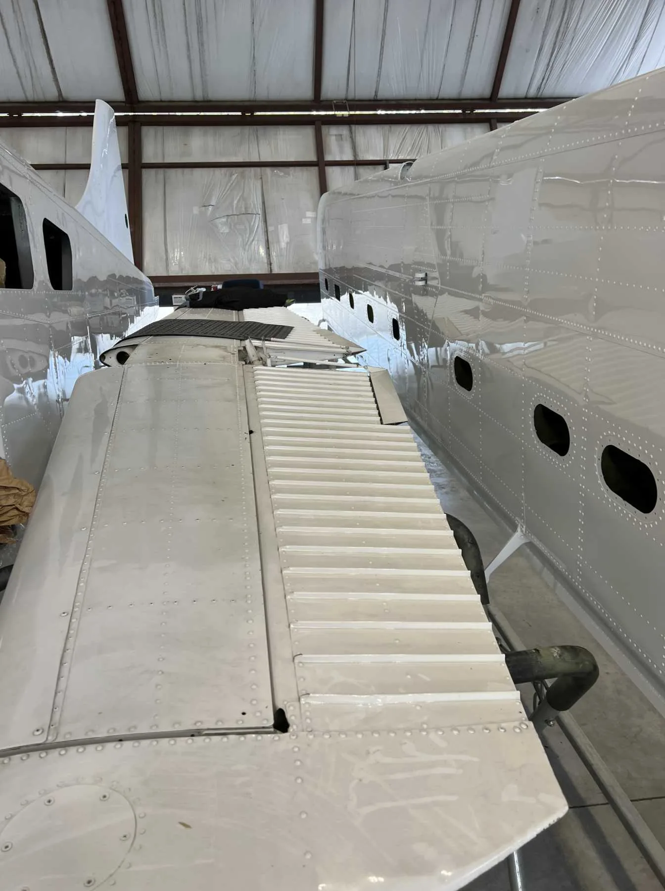 A close-up view of a white aircraft wing and fuselage sections, showing rivets and a step on the wing.